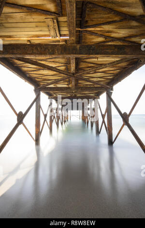 Visualizza in basso la spiaggia e l'oceano sotto la pesca del molo, fotografato qui con una lunga esposizione Foto Stock