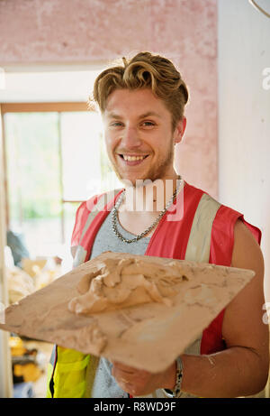 Ritratto sorridente, fiducioso giovane lavoratore edile intonacatura Foto Stock