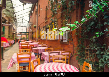 Concentrato uva selvatica lascia sullo sfondo della romantica estate outdoor cafe terrazza con panno rosso tavoli e sedie in legno. Horeca interior design co Foto Stock