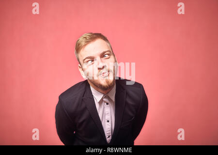 Un giovane uomo, 20-29 anni, in posa, espressione divertente, sporgersi in avanti. sfondo rosa, studio shot, photo shoot. faccia capo close-up, headshot. Foto Stock