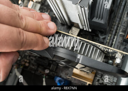 Uomo caucasico assemblaggio computer pc parti interne. Primo piano sulla scheda grafica e CPU dissipatore di calore del processore. Foto Stock