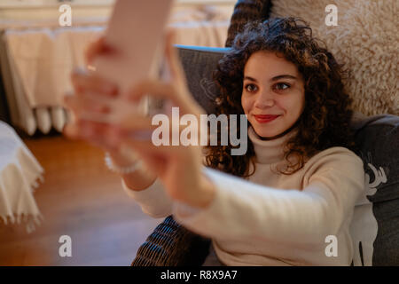 Sorridente bella giovane donna con capelli ricci sta prendendo un autoritratto Foto Stock