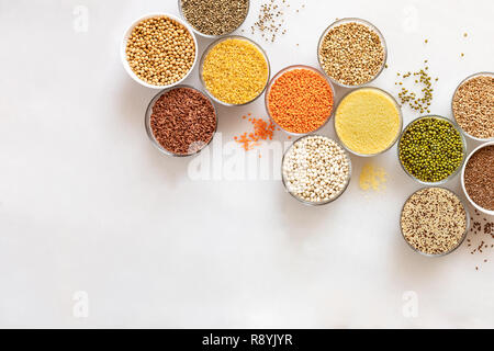 Diagonale laici piana ciotole in vetro con cereali, fagioli e semi su sfondo bianco con copia spazio. Foto Stock