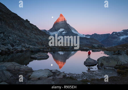 Escursionista su una roccia nel Riffelsee all'alba, godendo della vista sul Cervino. Foto Stock