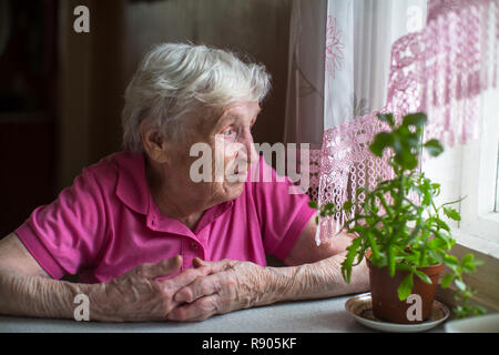 Donna anziana seduta al tavolo vicino alla finestra. Foto Stock