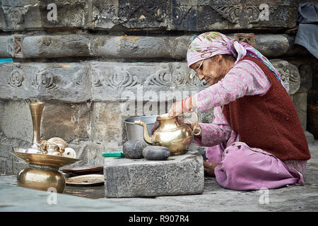 Naggar, India - 17 Luglio: vecchia donna Indiana che pulisce i piatti fuori del tempio. Piatti speciali che fanno offerte a Dio nel tempio. Luglio 17, 2013 Foto Stock