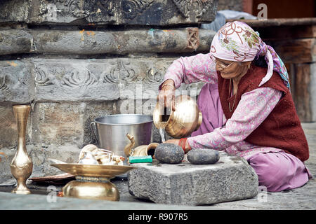 Naggar, India - 17 Luglio: vecchia donna Indiana che pulisce i piatti fuori del tempio. Piatti speciali che fanno offerte a Dio nel tempio. Luglio 17, 2013 Foto Stock