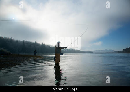 Silhouette del pescatore di Pesca a Mosca Report di Pesca del salmone e mare eseguire tagliagole trota in Puget Sound vicino a Olympia, Stati Uniti di Washington. Foto Stock