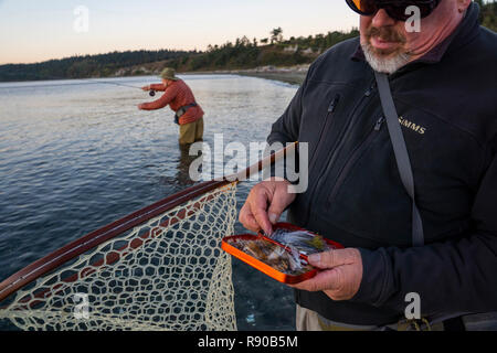 Un fly-guida di pesca controlla il suo assortimento di Mosca per il salmone e costiere searun tagliagole trote mentre il suo cliente fly pesci in background. Foto Stock