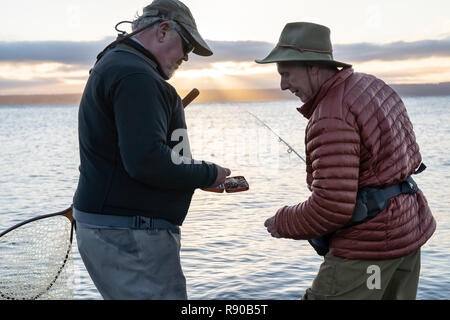 Un maschio di pescatore a mosca guarda il suo lavoro di guida mettendo su un nuovo volo per tentare di salmone e trota a acqua salata Spiaggia. Foto Stock