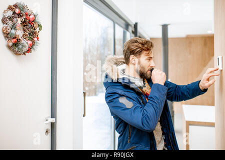 Uomo in abbigliamento invernale sensazione di freddo in camera di regolazione di temperatura con termostato elettronico a casa Foto Stock