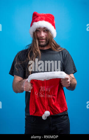 Ritratto o ventola indossando santa hat sorridente alla telecamera stupiti whil tenendo il sacco. Vacanze di Natale in concetto di pubblicità Foto Stock