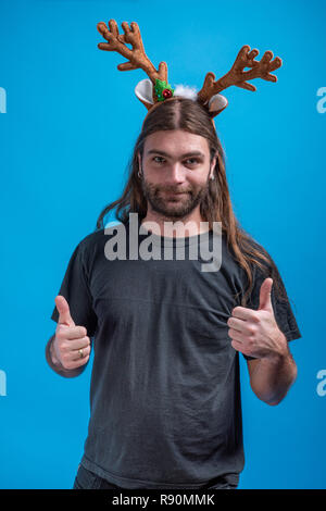 Indossare maschio raindeer fascia per capelli che mostra Thumbs up con entrambe le mani. Visualizzazione happy funny sentimenti Foto Stock