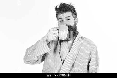 Uomo con barba e baffi mantiene la tazza di caffè isolato su bianco. Caffè del mattino concetto. Macho in accappatoio bevande di tè o caffè con la faccia del sonno. Guy guarda assonnato, necessita di caffè. Foto Stock