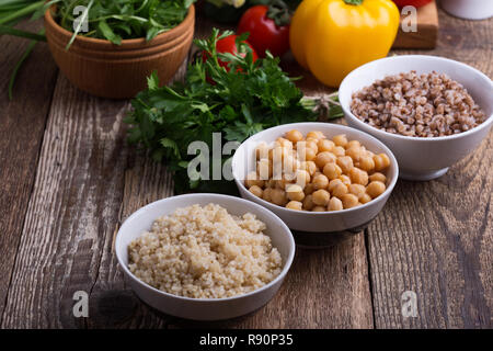 E una selezione di fresche verdure e cereali cotti, cereali e legumi, pianta sana base alimentare vegano. Ceci, quinoa e grano saraceno in ciotole su rusti Foto Stock
