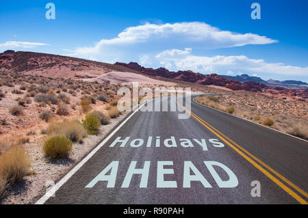 Il testo "Vacanze a venire" scritto su una strada vuota nel deserto del Nevada prima la strada gira a destra Foto Stock