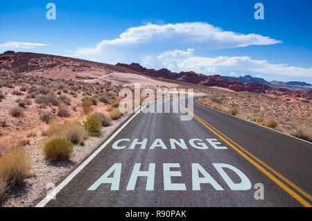 Il testo 'Change ahead' scritto su una strada vuota nel deserto del Nevada prima la strada gira a destra Foto Stock