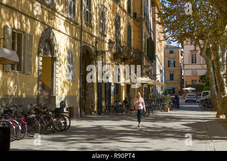 Lucca, Italia: Piazza Napoleone, Donna che cammina nel sole pezzata Foto Stock