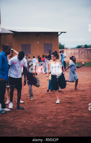 Mali, Africa - una giovane donna caucasica stretching con africano nero bambini, ragazzi e adulti per giocare a calcio in una discarica per rifiuti. Area rurale vicino a Bamako Foto Stock