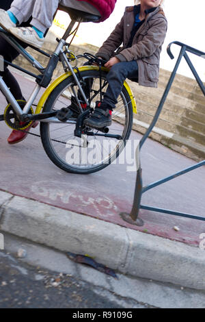 Vista ritagliata di due bambini piccoli a cavallo di una vecchia bicicletta essendo spinto dalla loro madre lungo un marciapiede della città di Montpellier, Francia Foto Stock