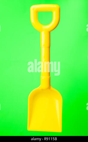 Una plastica gialla vanga giocattolo contro uno sfondo verde Foto Stock