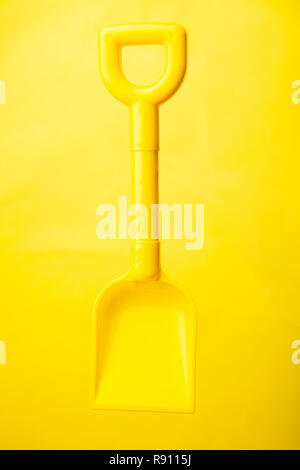 Una plastica gialla vanga giocattolo contro uno sfondo giallo Foto Stock