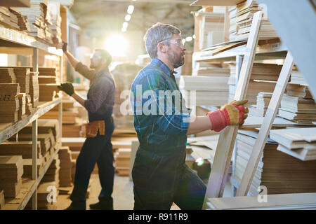 Grey-haired lavoratore manuale controllo assi di legno a magazzino Foto Stock