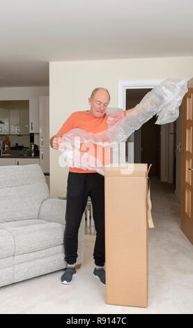 L'uomo disimballaggio un marrone scatola in cartone contenente una quantità eccessiva di aria di protezione sacchetti Foto Stock