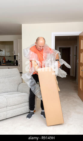 L'uomo disimballaggio un marrone scatola in cartone contenente una quantità eccessiva di aria di protezione sacchetti Foto Stock