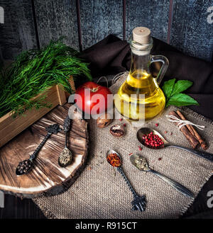 Bottiglia con olio e spezie varie in cucchiai sul tavolo Foto Stock