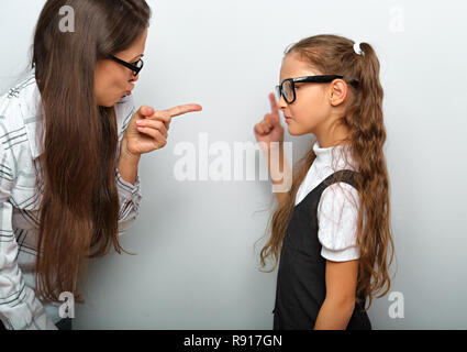 Arrabbiato bella donna di occhiali scolding allieva e figlia shwoung il dito su sfondo blu Foto Stock