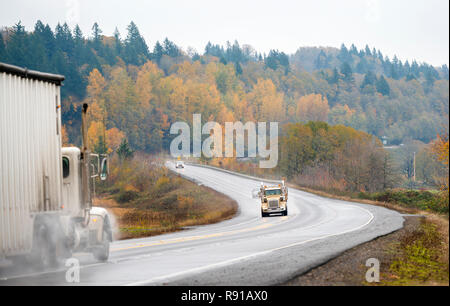 Due grandi piattaforme semi camion un suggerimento di carrello e uno con rimorchio bulk muoversi le une verso le altre sulla strada tortuosa sotto la pioggia meteo di prelevare il cloud di pioggia Foto Stock