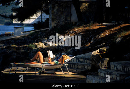 La donna posa su una sedia a sdraio in costume da bagno la lettura di un libro, Bozava, Dugi otok croazia Foto Stock