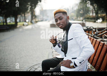 Chic bello african american uomo in abito bianco seduta sul banco di lavoro. Foto Stock