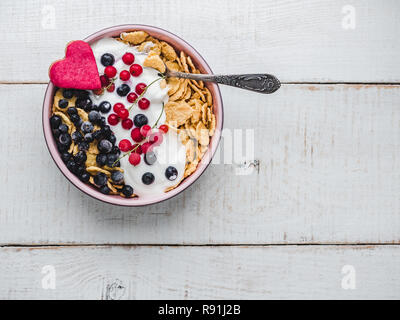 Una sana prima colazione. Biscotti di cereali in smalto di colore rosa, cereali, yogurt e frutti di bosco freschi sullo sfondo delle lavagne bianche. Close-up, vista dall'alto, isolato Foto Stock