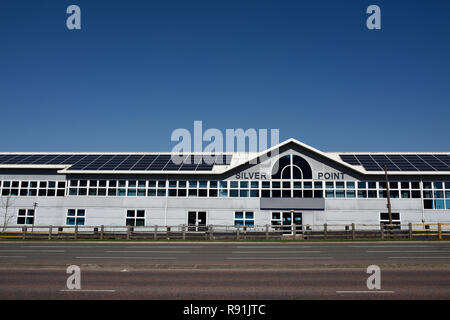 Pannelli solari fotovoltaici montati sul tetto di un moderno edificio commerciale, strada vuota, nessun traffico in primo piano, cielo blu chiaro, a Bury lancashire uk Foto Stock