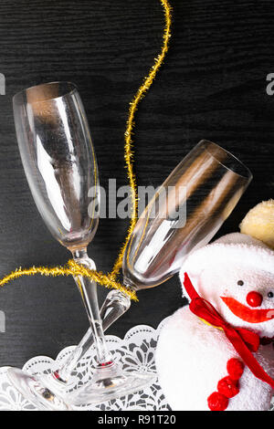 Due bicchieri di champagne decorate con Natale pupazzo giocattolo e un nastro di oro su sfondo di legno. spazio copia Foto Stock