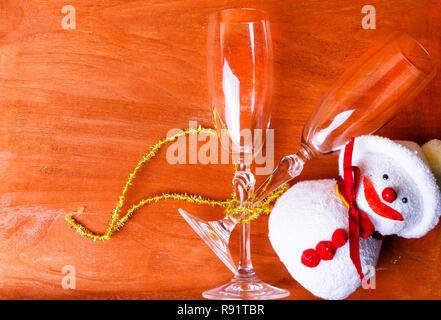 Due bicchieri di champagne decorate con Natale pupazzo giocattolo e un nastro di oro su sfondo di legno. spazio copia Foto Stock