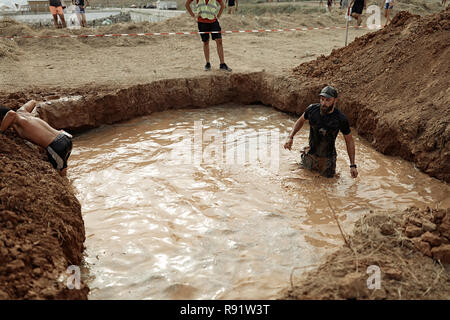 Forte giovane con muscoli passando attraverso la piscina con acqua sporca.abbigliamento sportivo nero sul suo corpo, orologi subacquei sul braccio.concorrenza duro Foto Stock