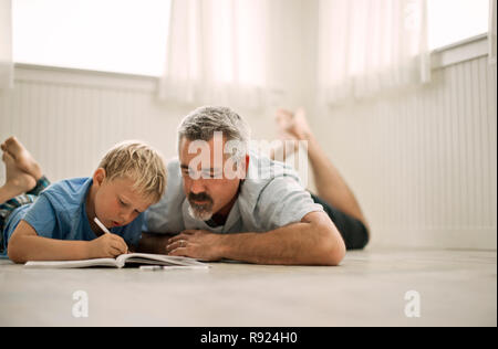 Adulto uomo disteso sul pavimento aiutando il suo figlio con i compiti. Foto Stock