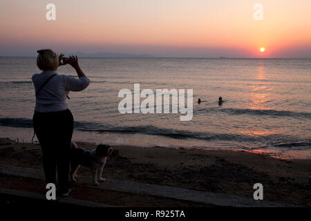 Donna prendendo fotografare il tramonto sul mar egeo vouliagmeni Atene Attica Grecia Foto Stock