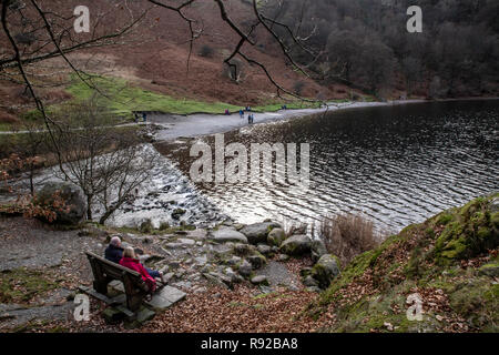 Un paio di rilassarvi su una panchina e godere il paesaggio all'estremità meridionale del lago di Grasmere dove l'acqua scorre su uno stramazzo nel fiume Rothay. Foto Stock