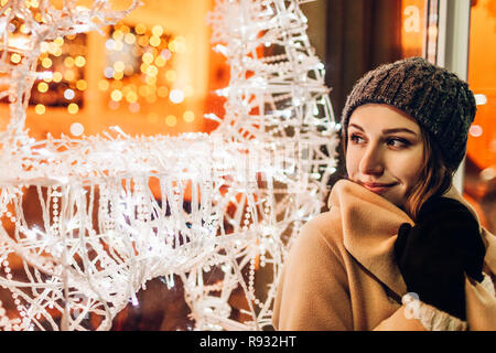 Giovane donna a piedi in città e guardando decorate vetrine di Natale di notte. Anno nuovo concetto Foto Stock