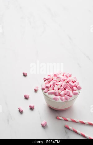 Cioccolata calda o di cacao con panna montata e rosa marshmallow candy in rosa e bianco mug con strisce rosa cannucce su marmo bianco tavola. Spazio di copia Foto Stock
