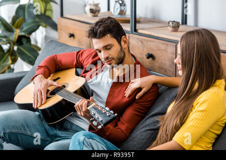 Giovane ragazza seduta sul divano con il mio ragazzo mentre si ascolta la musica per chitarra Foto Stock