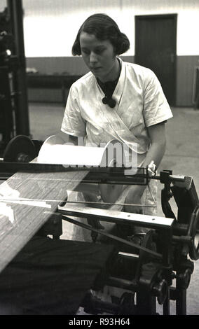 1940s, storico, un giovane adulto lavoratore di sesso femminile che in un bianco-coat operando una macchina tessile in una fabbrica, South Wales, Regno Unito. L'introduzione di luce industria manifatturiera a Merthyr area dopo WW2 portato all'impiego di un maggior numero di donne, in contrasto con il declino delle industrie pesanti di carbone e di acciaio che impiegate principalmente uomini e vide i numeri di arge di loro disoccupati nel Galles del Sud in questa epoca. Foto Stock