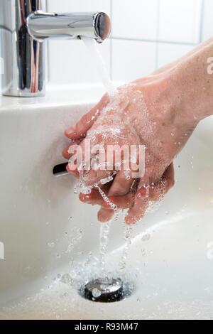 Persona di lavare le mani sotto l'acqua da un rubinetto, immagine simbolica per il consumo di acqua Foto Stock