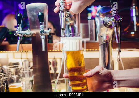 Giovane donna erogazione birra nel bar dalle imboccature di metallo. Bella barista toccando la birra nel bar. Foto Stock