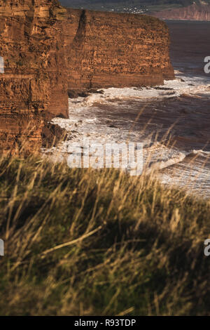 Onde si infrangono in rosso scogliere di arenaria della Jurassic Coast, East Devon, Sud Ovest dell'Inghilterra, Regno Unito. Foto Stock