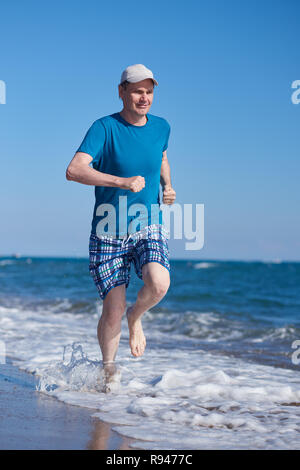 A piedi nudi uomo maturo durante il jogging sulla spiaggia Foto Stock